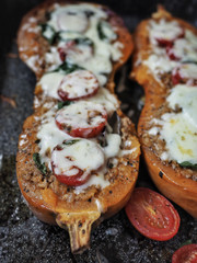 Baked halves of pumpkin stuffed with crushed meat, tomatoes and cheese. Seasonal meal.
