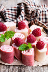 Rolled milk and raspberry pancakes on wooden table