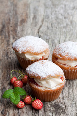Cupcakes stuffed with white cream and wild strawberry on wooden table