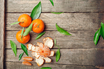 Tangerines (oranges, clementines, citrus fruits) with green leaves over wooden background with copy space