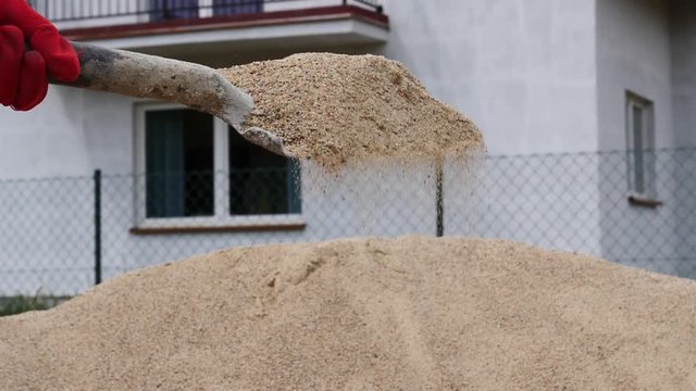 Worker with shovel work at construction site, hand holding scoop full of building sand. Sand falls from spade in slow motion. Detail view, closeup