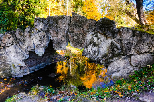 Beautiful autumn sunny landscape in Pavlovsk park with the old stone bridge over creek, and trees with red and orange leaves, Pavlovsk.