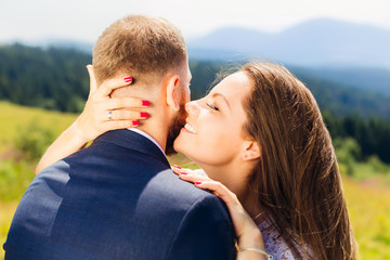 the bride has closed her eyes and whispers something to her groom and hugs him around the neck and shoulders on the background of the mountains