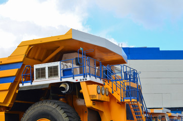 View of the cab of the world's largest yellow mining truck against a blue sky with white clouds