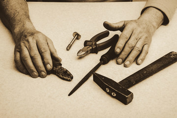 Table composition with tools (nippers, hammer, pliers, rasp, bolt) and hands of elderly working man...