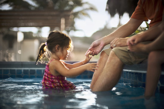 girl in pool holding father?s hand