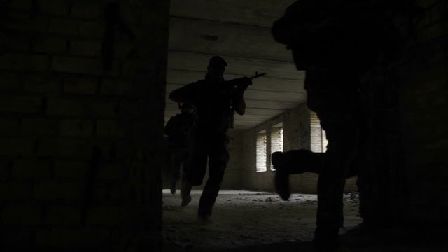 Squad of fully equipped and armed soldiers running through abandoned building captured by enemy during rescue operation. Special forces marines storming enemy positions during anti terrorism operation