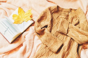 Flat lay autumn photo. Brown woolen sweater, open book and yellow maple leaf on a bed