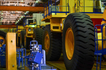 Line, conveyor for the production of large yellow career dump trucks, mining trucks. Shop factory. Huge tires with rims