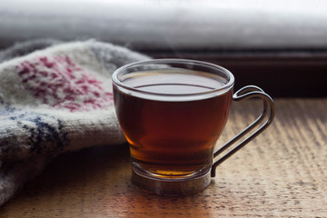 Glass Cup with tea on wooden background, close gloves with ornament