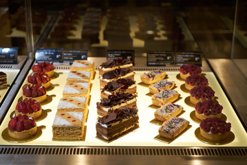 Cake shop with sweets on showcase table, close-up. Different types of cakes pieces in pastry shop glass display