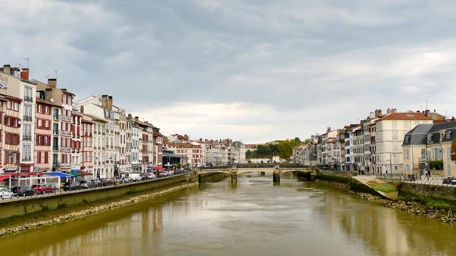 The Pannecau bridge is a Bayonne footbridge that crosses the Nive river. On either side of the shoreline, there are typical old houses. Filmed in a cloudy day.