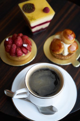 Breakfast time with cup of hot coffee and pieces of cream cake with strawberries and raspberries, sweets dessert breakfast snacks, close-up. Berry cupcakes dessert on wooden table background, top view