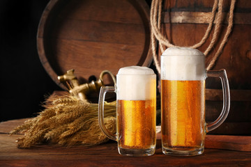Two mug of beer .With wheat and barley and barrels spikes on bakcground.Still life