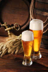 Two glass of beer .With wheat and barley and barrels spikes on bakcground.Still life