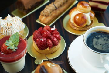 Breakfast time with cup of hot coffee and pieces of cream cake with strawberries and raspberries, sweets dessert breakfast snacks, close-up. Berry cupcakes dessert on wooden table background, top view