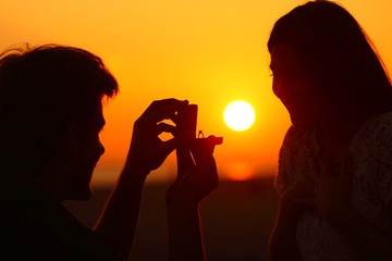 Marriage proposal at sunset with sun in background - obrazy, fototapety, plakaty