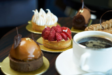 Breakfast time with cup of hot coffee and pieces of cream cake with strawberries and raspberries, sweets dessert breakfast snacks, close-up. Berry cupcakes dessert on wooden table background