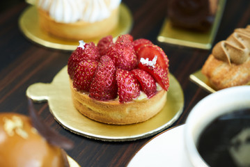 Breakfast time with cup of hot coffee and pieces of cream cake with strawberries and raspberries, sweets dessert breakfast snacks, close-up. Berry cupcakes dessert on wooden table background