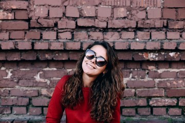  stylish young woman in red dress and sunglasses on brick wall background. fashionable long-haired girl