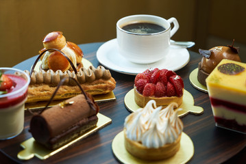Morning breakfast time with cup of hot coffee and pieces of cream cake with strawberries and raspberries, sweets dessert breakfast snacks, close-up. Berry cupcakes dessert on table background