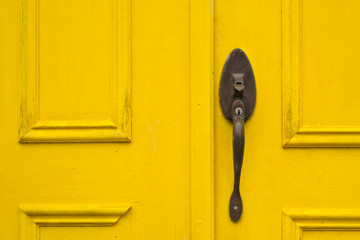 Sectional view of rustic exterior yellow wooden door and handle.