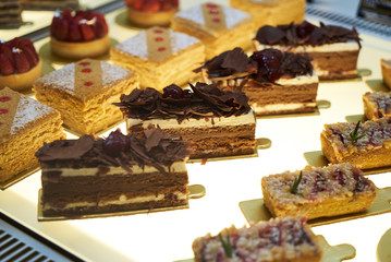 Cake shop with sweets on showcase table, close-up. Different types of cakes pieces in pastry shop glass display