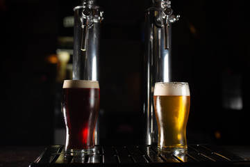 Two pint glasses of beer, a golden one and a dark one on the bar tab.