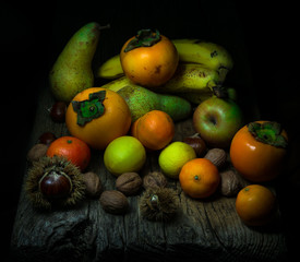Natura morta con frutta mista: noci, marroni/castagne, mandarini, limoni, cachi/diosperi, mele, pere e banane su tavolo di legno