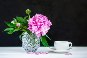 Cup of tea and peonies in a vase on the table.