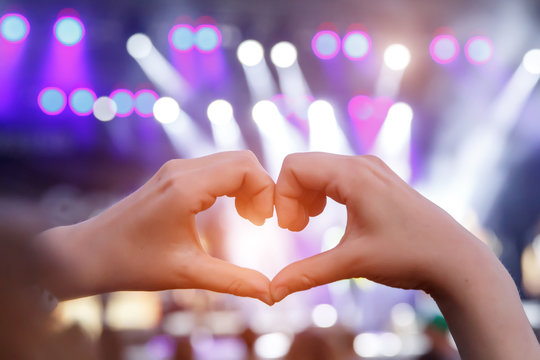 Girl making a heart-shape symbol for her favorite band on concert