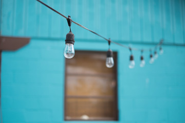 LIGHT BULBS ON STRING WIRE WITH BLUR GREEN HOUSE BACKGROUND .