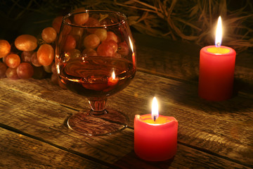 christmas candles, grapes and glass with cognac or whisky on wood background. Christmas decoration.