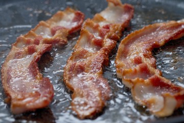 CLOSE UP IMAGE OF BACON BEING FRIED IN PAN - DELICIOUS BUT UNHEALTHY