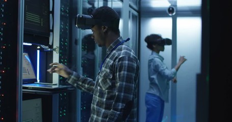 African American colleagues wearing VR glasses while working with hardware in server room data center - Powered by Adobe