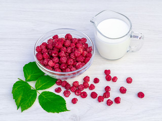 Fresh raspberries in a glass bowl and natural iogurt on a white wooden table. Healthy eating concept