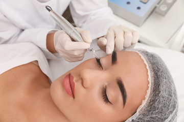 Obraz na płótnie Canvas Young woman undergoing procedure of permanent eye makeup in tattoo salon, closeup