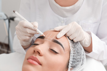 Fototapeta premium Young woman getting prepared for procedure of permanent eyebrow makeup in tattoo salon, closeup