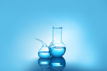 Laboratory glassware with liquid on table against color background. Chemical analysis