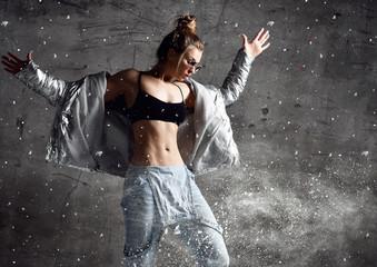 Woman workout exercise stand in silver sexy down puffer jacket blue jeans sunglasses on loft wall with dust snow splashes © Dmitry Lobanov
