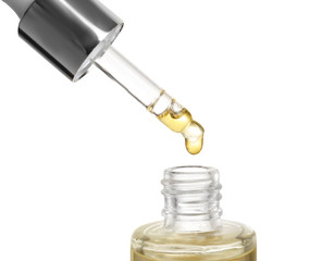Dripping essential oil from pipette into glass bottle on white background