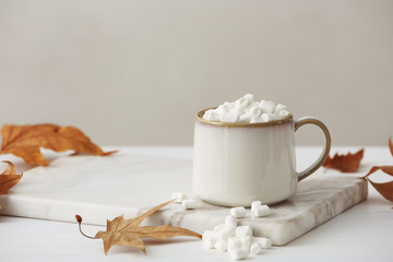 Cup of hot cozy drink with marshmallows and autumn leaves on table. Space for text