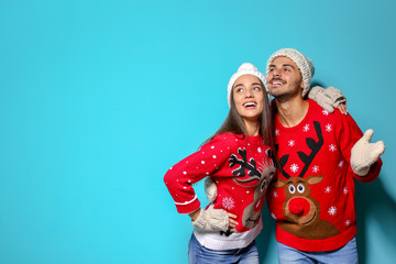 Young couple in Christmas sweaters and knitted hats on color background. Space for text
