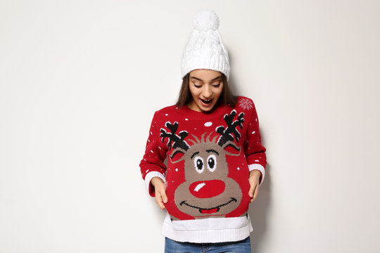 Young woman in Christmas sweater and knitted hat on white background