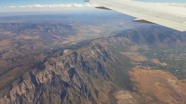 POV-Aircraft wing flying over rugged mountains and northern cities of Utah's Wasatch Front as aircraft descends for landing at Salt Lake City