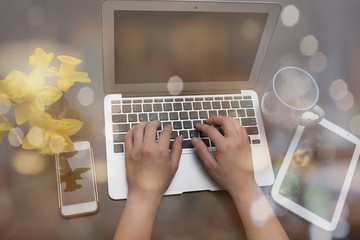 WOMAN TYPING KEYBOARD OF A LAPTOP / NOTEBOOK SURROUNDING BY COFFEE CUP,  TABLET,  AND YELLOW DAFFODIL IN A VASE  WITH NICE BLUR BOKEH LIGHT OVER THE IMAGE. (WORKING TECHNOLOGY AND BUSINESS CONCEPT)