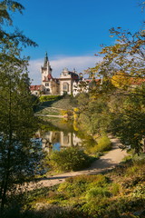 Fototapeta na wymiar Vertical image of romantic park and famous castle Pruhonice, Czech Republic, Europe, standing on a hill above lake, colorful sunny autumn day, blue sky, footpath along lake, reflection, vertical image