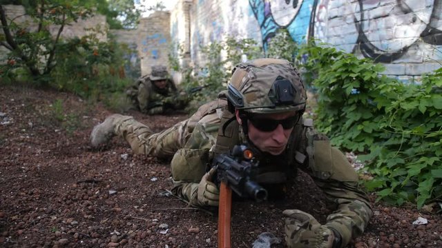Special forces marines with weapons and tactical devices crawling toward an enemy position during military training. Squad of soldiers sneaking up in enemy territory during anti terrorism training.