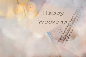 HAPPY WEEKEND NOTE ON A BOOK WITH COPY SPACE FOR TEXT SURROUNDED WITH CANDLES, A PEN , AND SMOKE / FOG EFFECT
