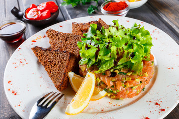 Tartar with salmon and avocado decorated with greens on plate on wooden table. Delicious appetizers